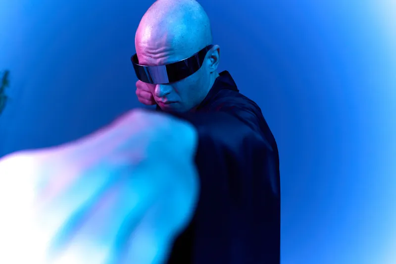 Muscular man in futuristic attire poses dramatically under bright blue lighting, showcasing determination and strength in a captivating black and white style.