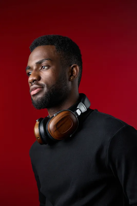 Portrait of a young Black man wearing stylish headphones, showcasing confidence against a vibrant red background, perfect for music and technology themes
