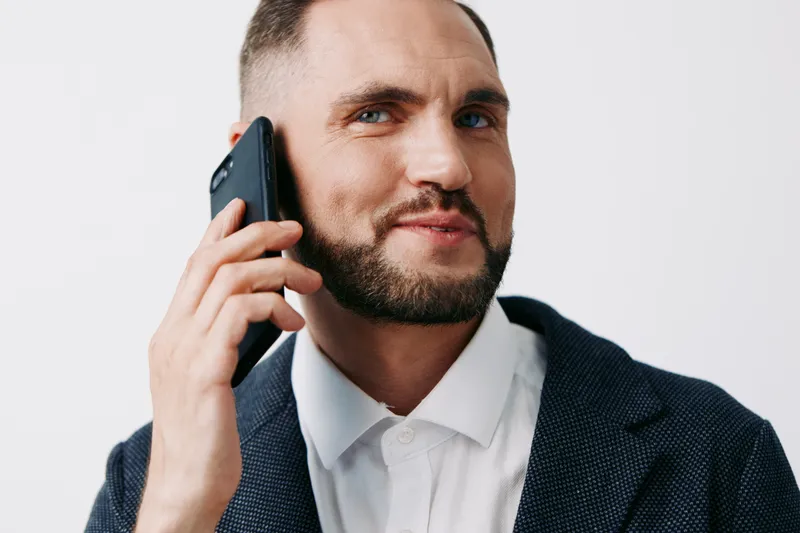 A confident business professional man on the phone, wearing a dark blazer and white shirt, with a friendly, focused expression against an isolated white background.