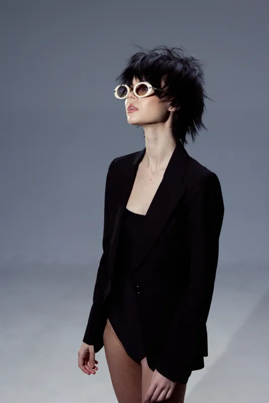 Stylish woman wearing sunglasses and black blazer with confident pose and modern edgy haircut.