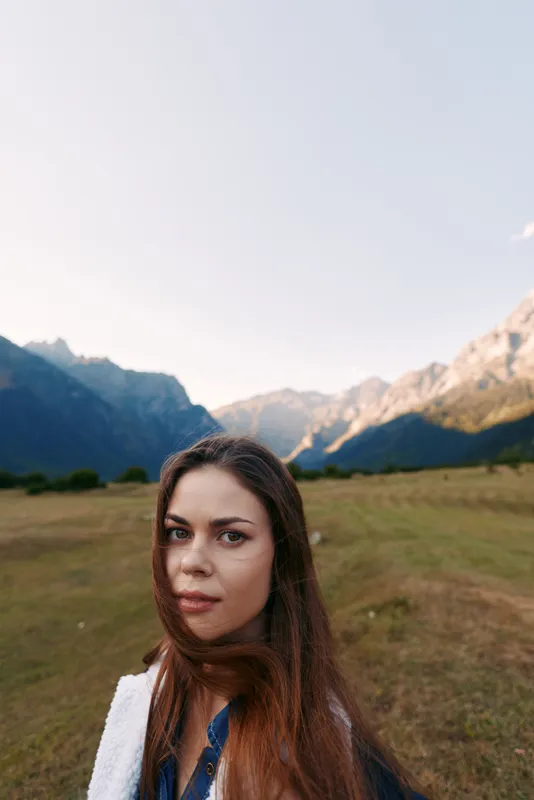 Woman portrait in mountains meadow nature landscape outdoors traveler looking at camera with long hair and soft light, scenic valley background for travel, adventure and calm mood.