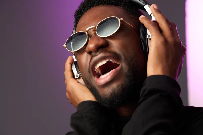 Young Black man enjoying music with headphones, expressing joy and passion, stylish sunglasses, modern background with vibrant colors