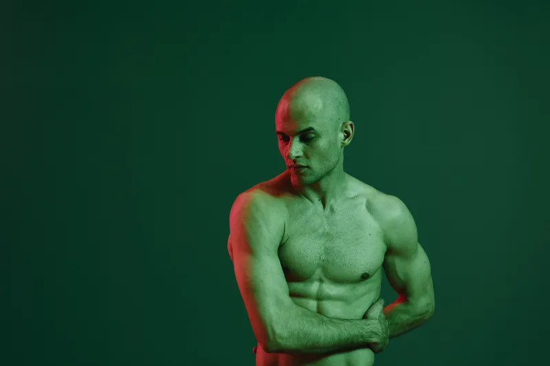 Reflective man showcasing strength and determination in a green light setting, emphasizing his physique in a bold and artistic manner.