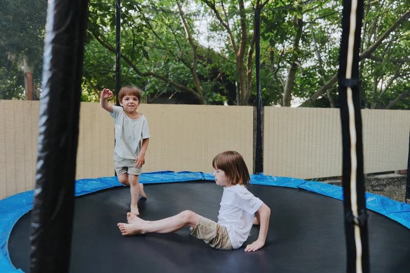Happy children playing on the trampoline in a sunny backyard, enjoying their time outdoors and having fun together in a joyful atmosphere.