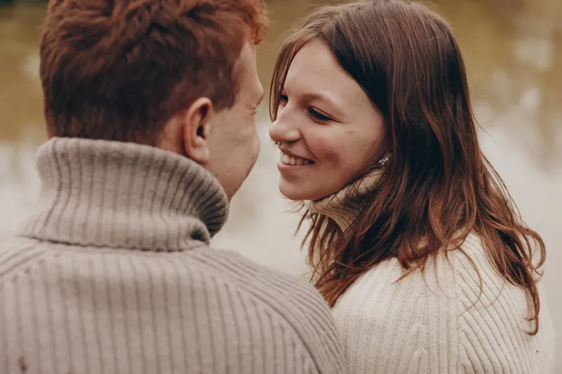 Couple romance outdoors sweater smiling connection warmth candid nature scenery, lifestyle moment of togetherness in cozy outfits under soft autumn light, capturing a relaxed intimate mood and