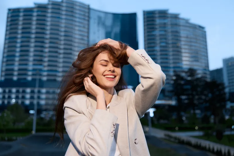 Confident businesswoman in a smart blazer enjoying her success outdoors, with modern architecture in the background, capturing a moment of joy and empowerment.