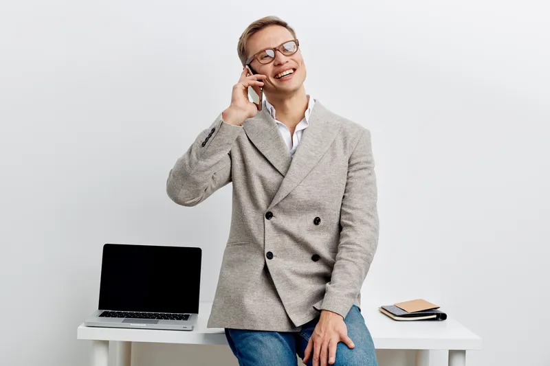 smiling man talking phone casual blazer glasses sitting laptop notebook white background work in metaverse digital nomad concept