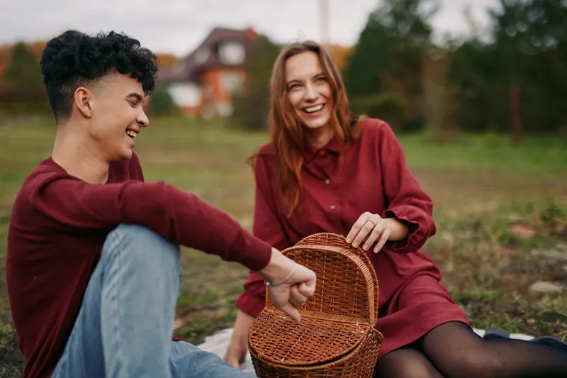 Authentic moment as two friends share a lighthearted picnic outdoors, genuine smiles, simple joy, and a candid connection captured in natural light and open countryside