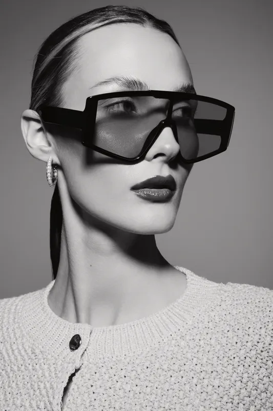 Close-up of a fair skinned Caucasian woman wearing oversized black sunglasses and a textured knitted sweater in black and white fashion portrait.