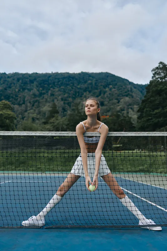 Young athletic girl preparing to serve on a tennis court with a scenic mountain background, exuding confidence and focus while wearing sporty attire