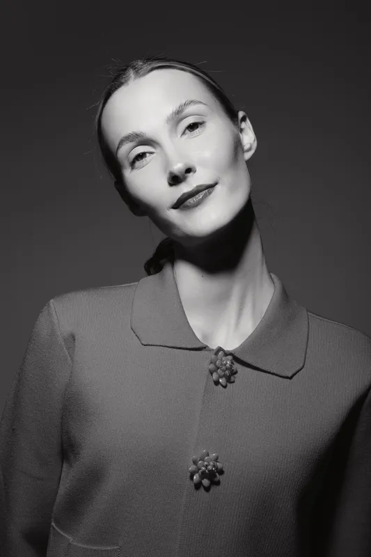 Portrait of a fair skinned Caucasian woman in vintage outfit looking at camera with soft expression in black and white studio photography.