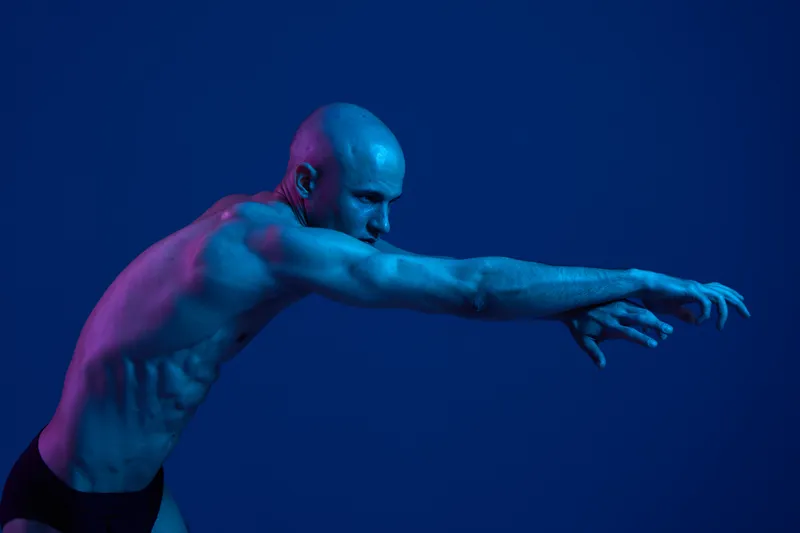 Athletic man in dynamic pose, showcasing strength and movement against a vibrant blue background. The image is full of energy and visual impact, perfect for fitness themes.