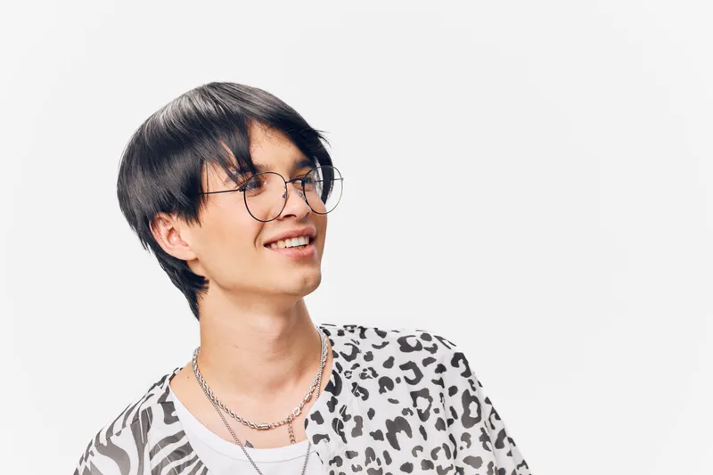 young man with glasses wearing a patterned shirt smiling looking sideways with a white background, casual style and joyful expression, studio portrait