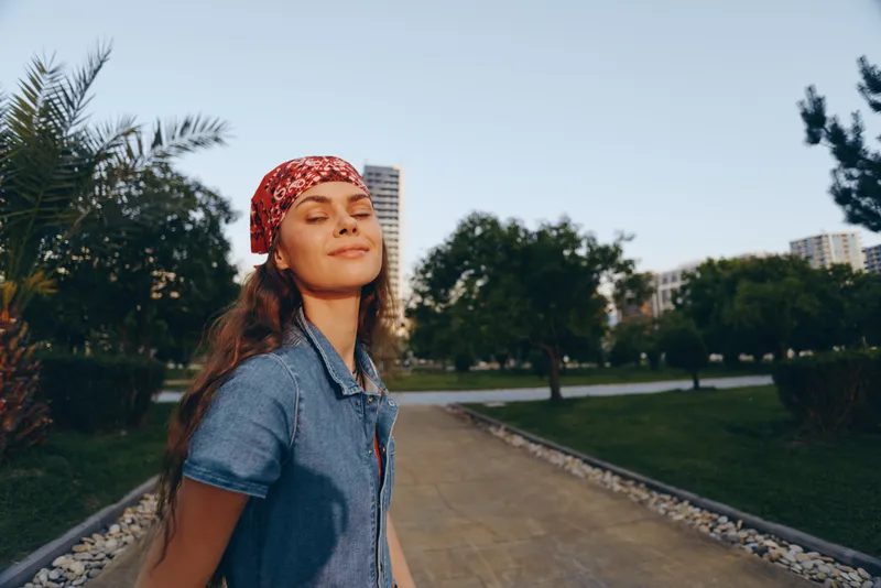 lifestyle woman in modern boho-western denim street style with bandana enjoying sunny day outdoors, film color tones highlighting relaxed and joyful mood
