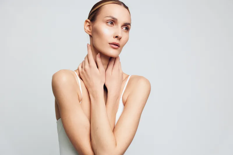 Woman portrait in studio light calm expression touch her face and cheek with hands smooth skin and natural makeup minimal beauty skincare concept soft shadows on neutral background
