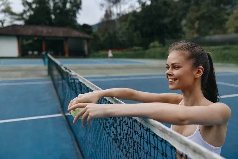Young athletic woman relaxing by tennis court, enjoying a moment of happiness and freshness green smoothie in hand, vibrant colors, and outdoor setting