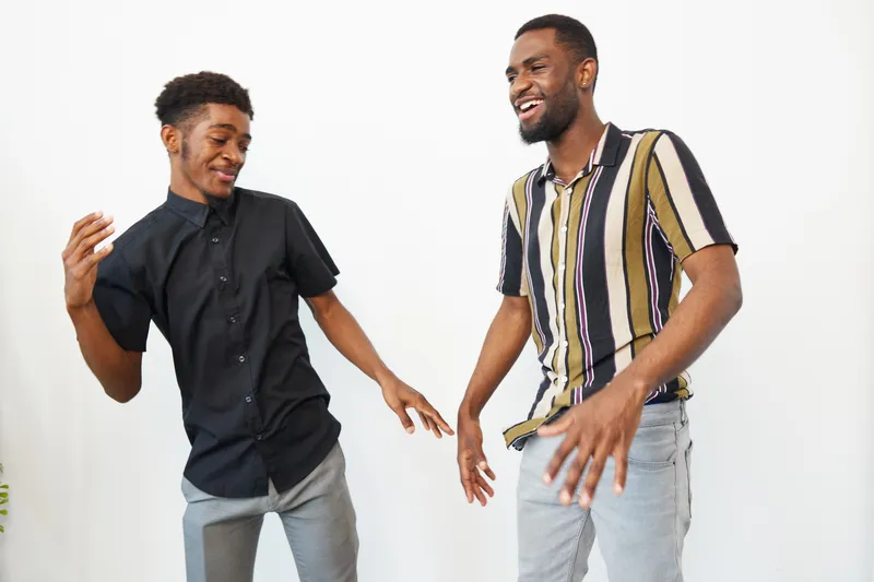 Two joyful black men dancing together, showcasing friendship and happiness in a bright, modern setting with contemporary clothing.