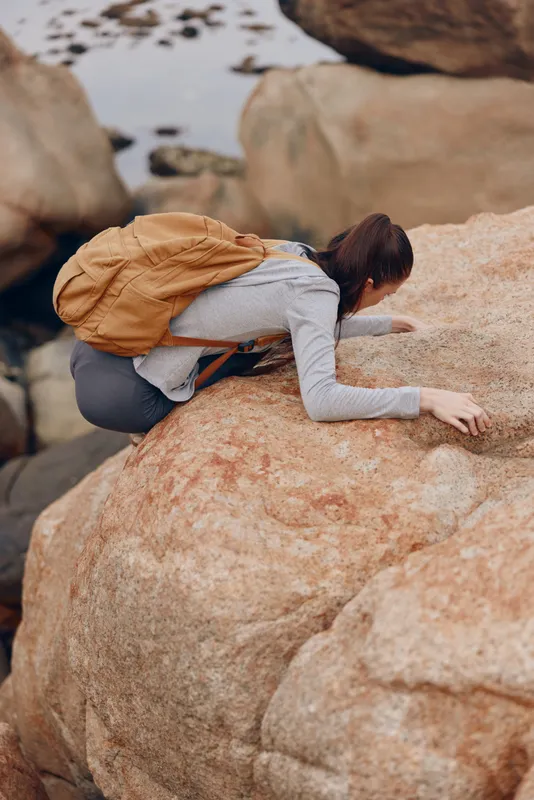 Young woman with brown backpack climbing on rocky terrain, showcasing determination and adventure in a natural outdoor setting