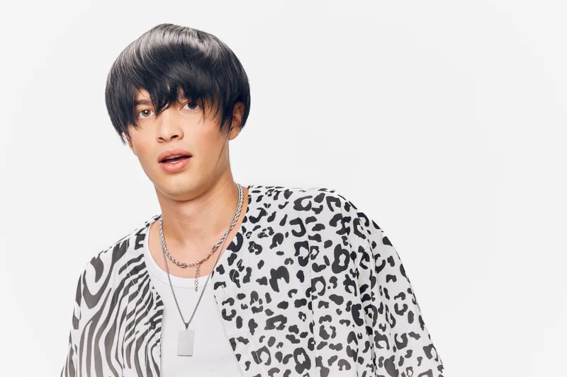 young man wearing animal print shirt and layered silver necklaces posing against white background with casual black hair style