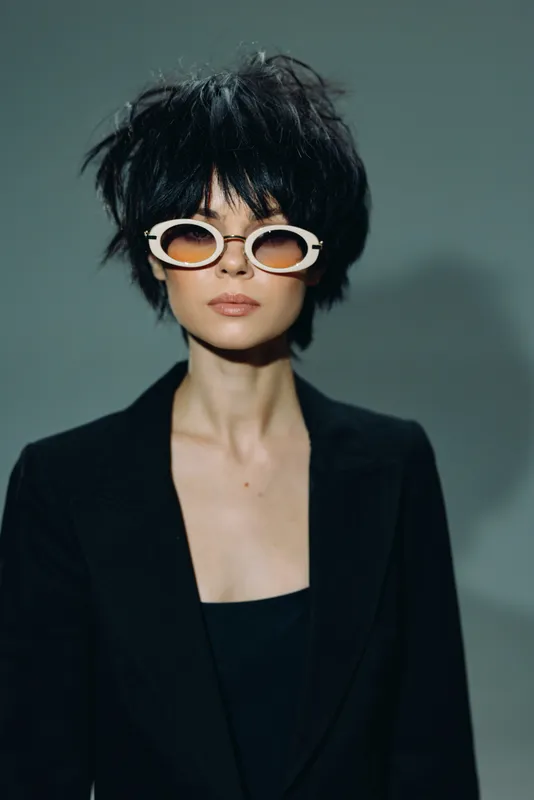 Stylish woman with short black hair wearing white sunglasses and a black blazer, exuding confidence and modern fashion elegance.