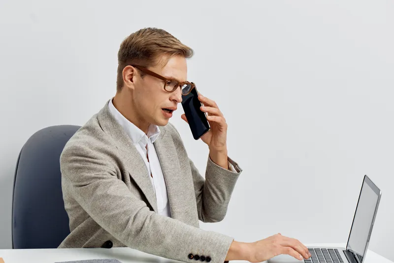 serious man talking smartphone using laptop work remotely freelance digital nomad casual wear glasses white background