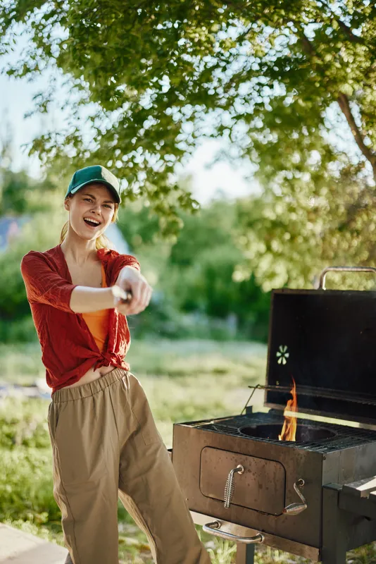 Joyful young woman in casual attire grilling outdoors in spring, showcasing a fun atmosphere and healthy lifestyle