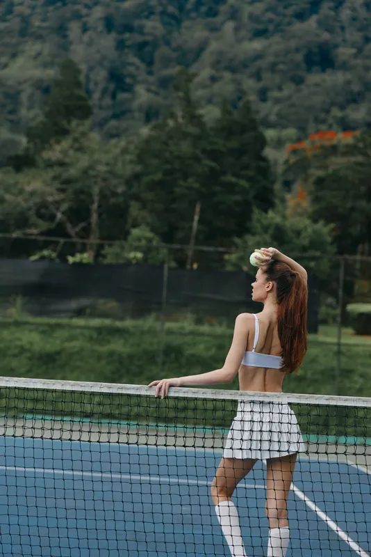 Young athletic woman in a sports outfit poses confidently on a tennis court, showcasing strength and determination in a vibrant outdoor setting
