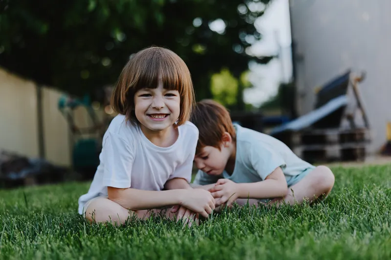 Happy children playing outside in the garden, surrounded by green grass and sunlight. Their joyful expressions highlight the beauty of childhood moments.