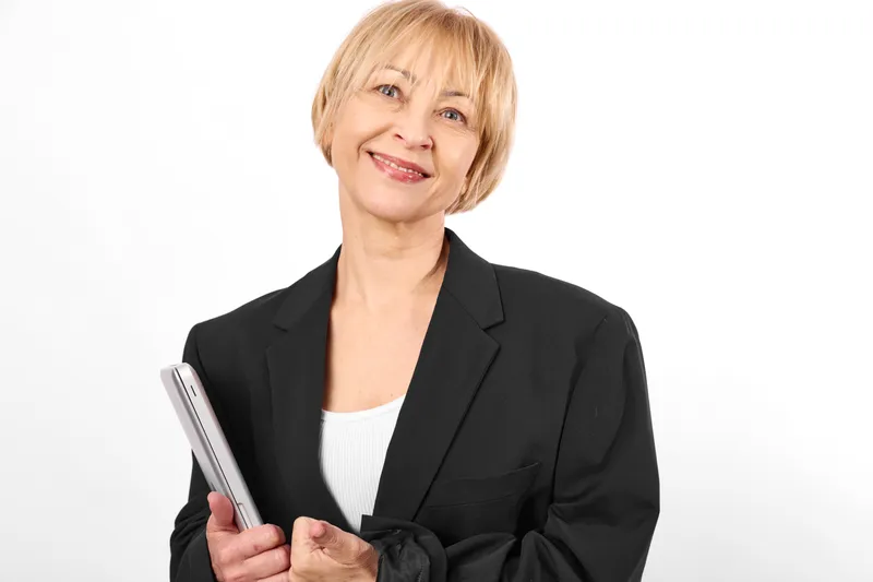 Smiling senior businesswoman portrait, black blazer, white shirt, holding pen, standing on white background, professional relaxed clean pose studio light