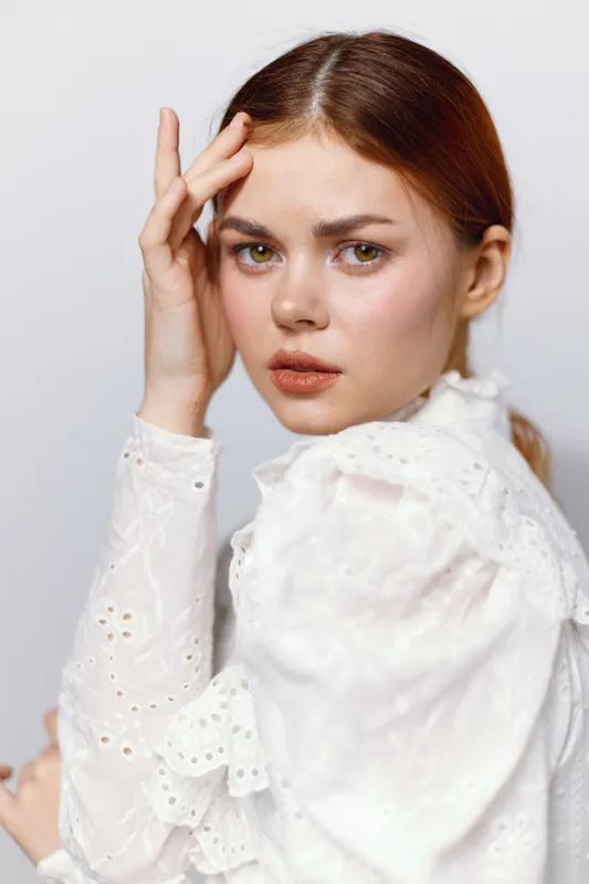 Emotional portrait of a young woman in a white blouse, expressing vulnerability against a neutral background, representing beauty and self reflection