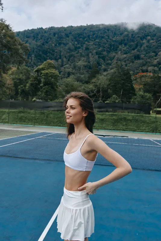 Young athletic female tennis player in white sportswear smiling on outdoor court surrounded by nature Healthy lifestyle, sportswoman, tennis action, nature background