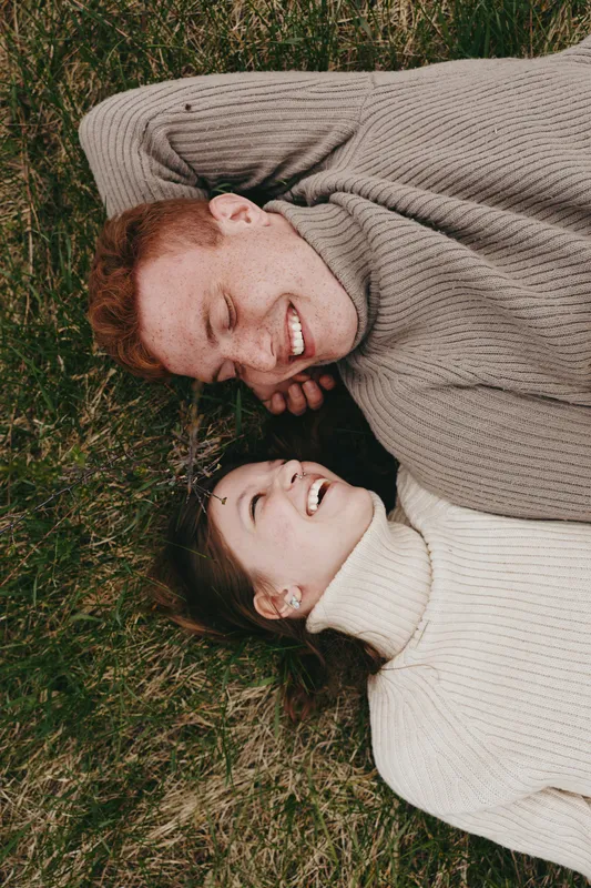 Couple smiling outdoors on grass wearing a sweater, cozy and intimate, relaxed mood captured in natural light, showcasing love, comfort, connection and happiness for lifestyle storytelling.