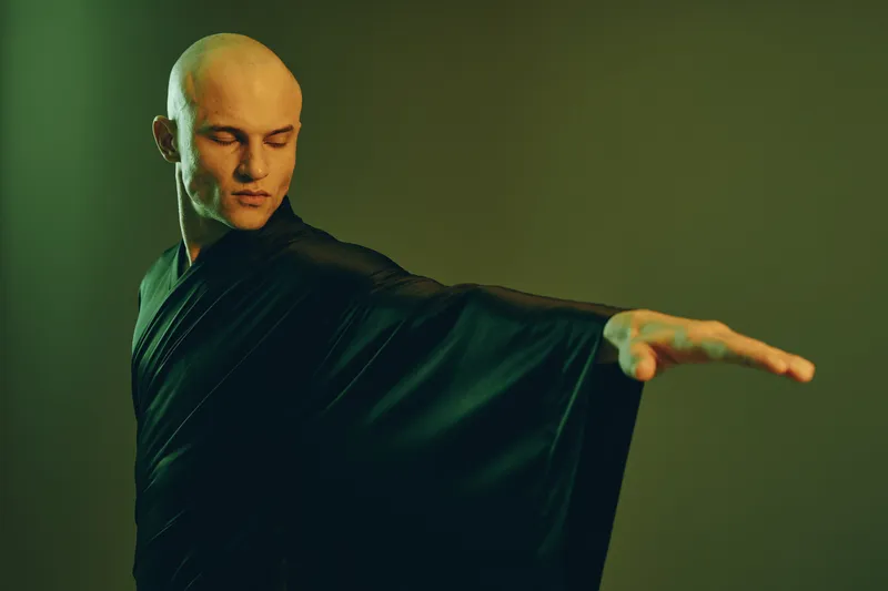 A focused man in a black robe gracefully extends his arm, showcasing elegance and poise in this captivating image. Perfect for themes of balance and serenity.