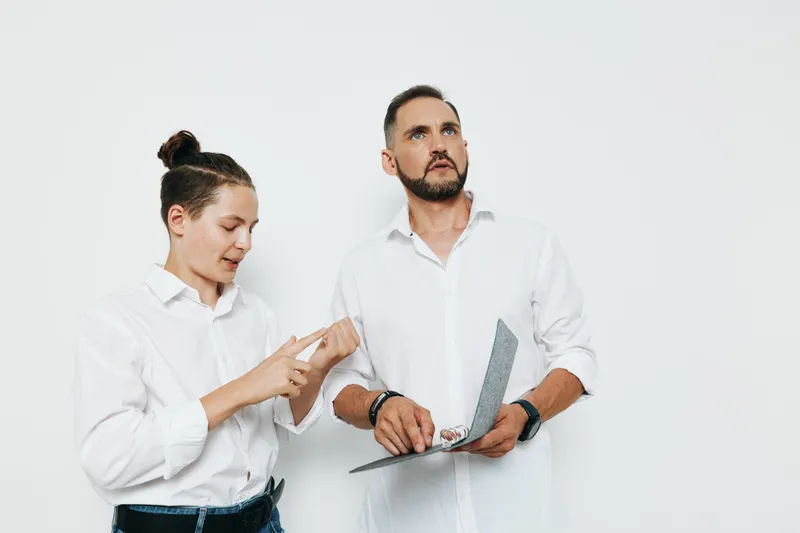 A business professional man stands beside a colleague against an isolated white background, showing focus, curiosity, and gentle collaboration in a polished corporate scene.
