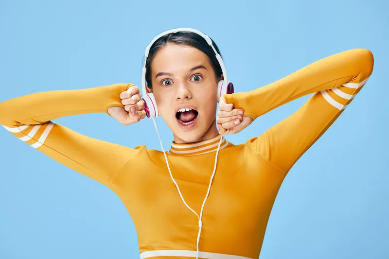 Athletic woman in orange sportswear with headphones, striking a dynamic pose and shouting with energy, ready for intense workout and sport training in a bright studio background.