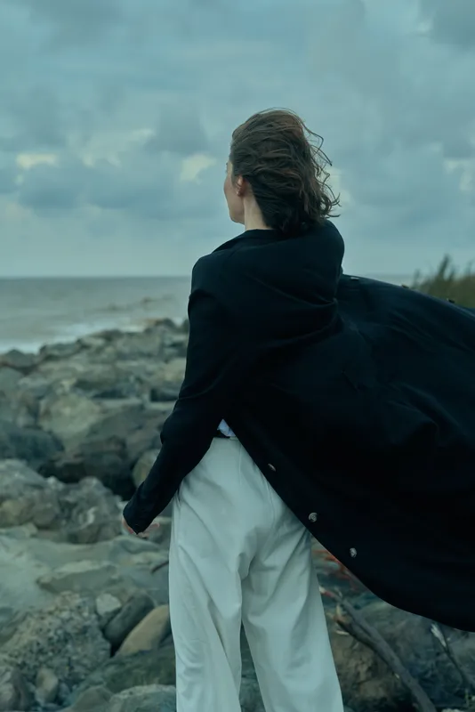 Wind, coat, shoreline, ocean, windblown silhouette in dramatic landscape style, outdoors fashion, breeze and stormy sky with rocks and seascape textures, windswept figure on coast in dramatic lighting