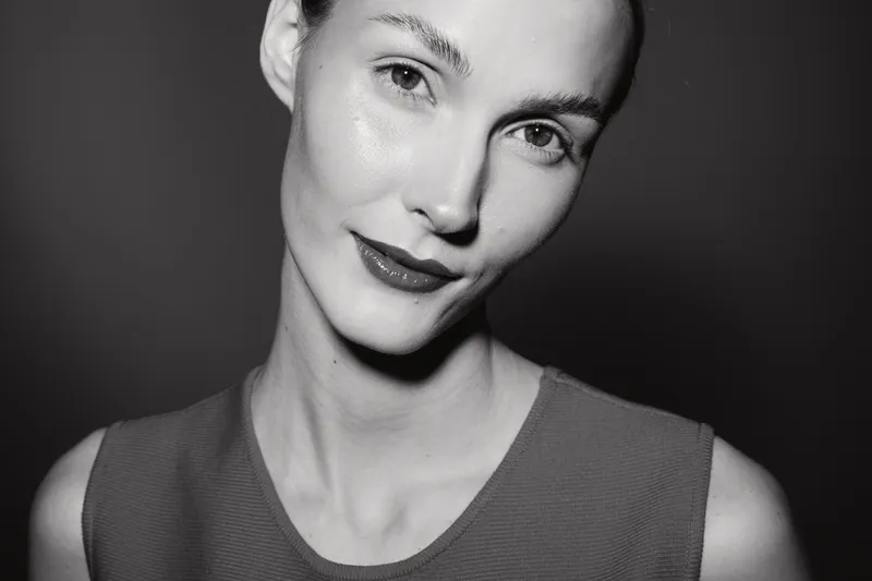 Portrait of a young Caucasian woman with fair skin and red lips smiling softly in black and white photo studio shot.