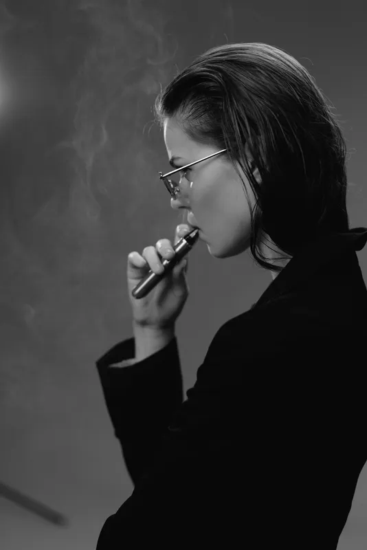 Black and white portrait of a thoughtful woman vaping with glasses indoor minimalistic style