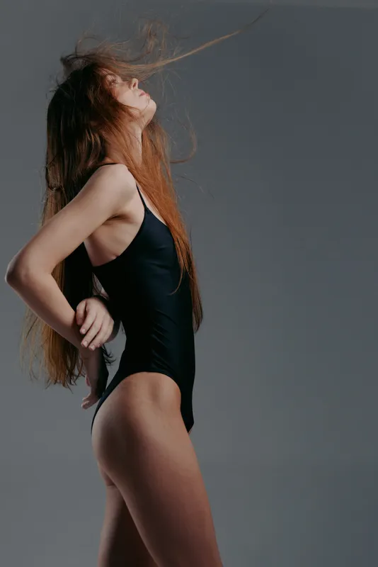 woman in black swimsuit with flowing hair on grey background, dynamic pose, long red hair, studio lighting