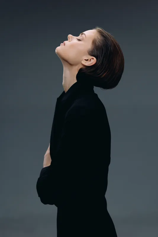 Profile of a thoughtful woman in black clothing with closed eyes on gray background