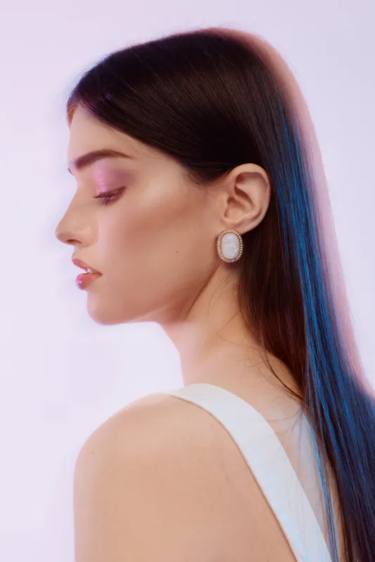 Profile of a young woman with long dark hair wearing elegant earrings and a white top. Soft lighting highlights her smooth skin and natural beauty. Fashion concept.