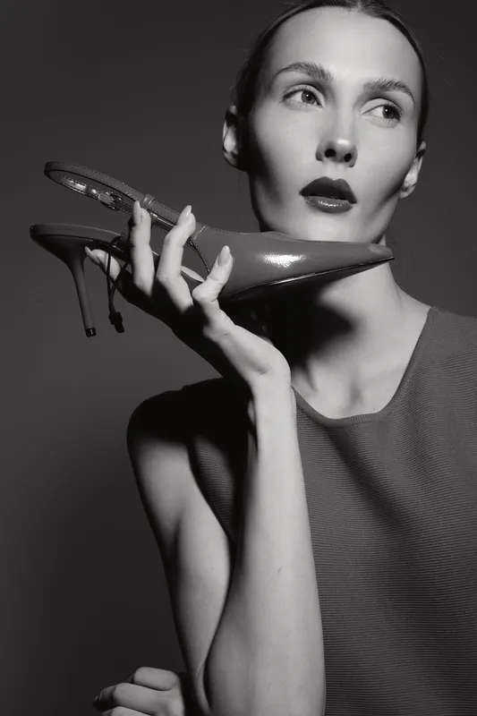 Portrait of a pale white woman with slicked hair holding a high heel shoe near her face in black and white. Concept for fashion, elegance, and beauty photography.