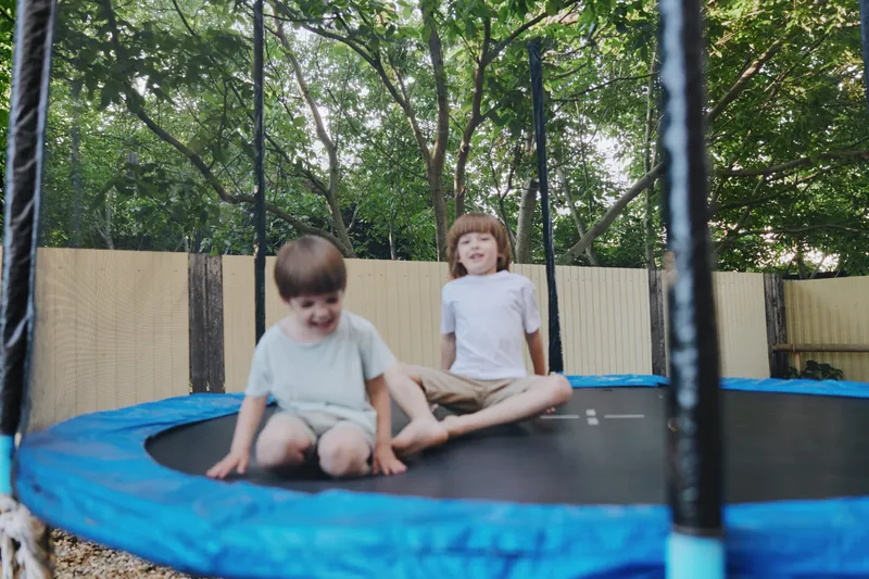 Happy children jumping on a trampoline, enjoying a sunny day outdoors, surrounded by greenery and laughter, experiencing the joy of play.