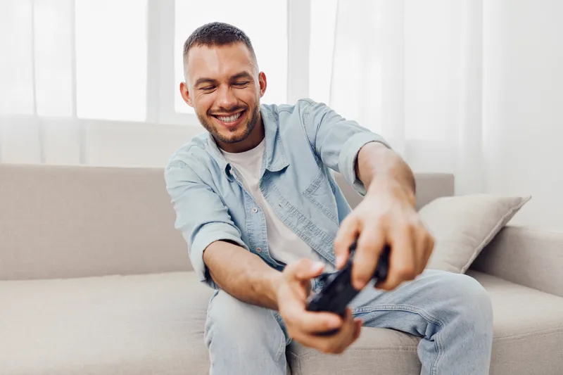 Happy man enjoying a video game in a cozy home environment, representing the balance between leisure and technology. Embracing life’s imperfections and solo living.
