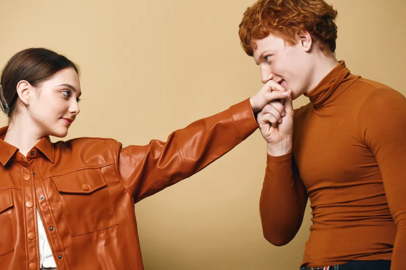 Couple, man and woman in casual clothes showing affection with hand kiss and look for romance and connection in relationship on beige background.