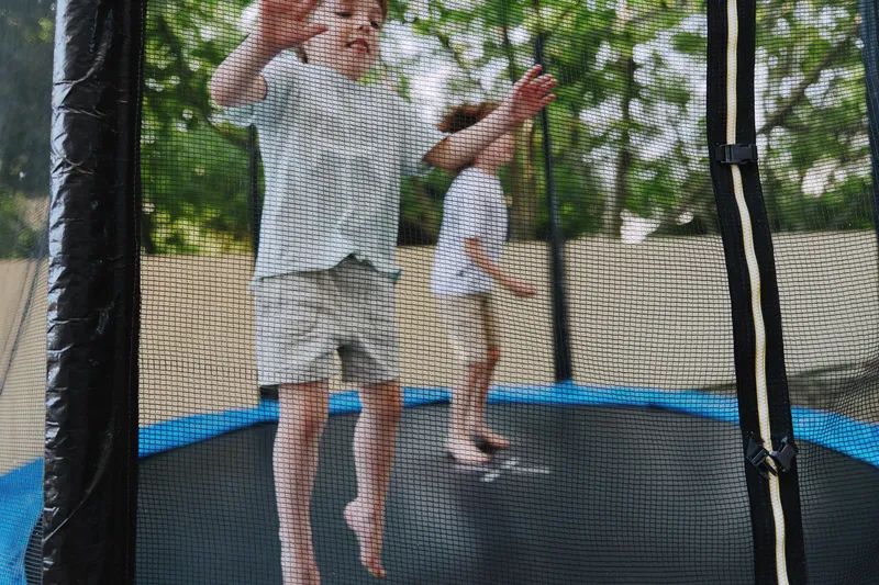 Happy children jumping on a trampoline, enjoying outdoor playtime surrounded by greenery and sunlight, creating joyful memories. ###