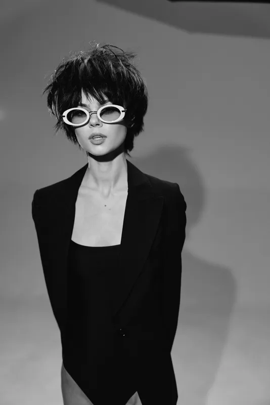 Stylish woman wearing white sunglasses and black blazer in black and white portrait.