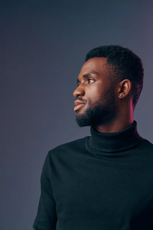Portrait of a confident young Black man in a stylish turtleneck sweater against a gradient background, showcasing modern fashion and elegance in character