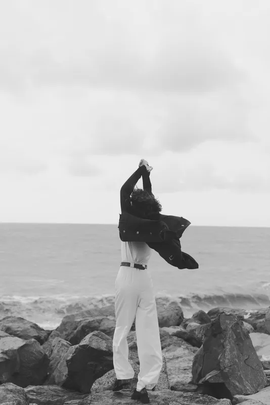 Sea breeze lifts a coat in a windy coastal scene, outdoor mood of freedom and movement on rocky shore, monochrome composition capturing rugged coastline and open horizon