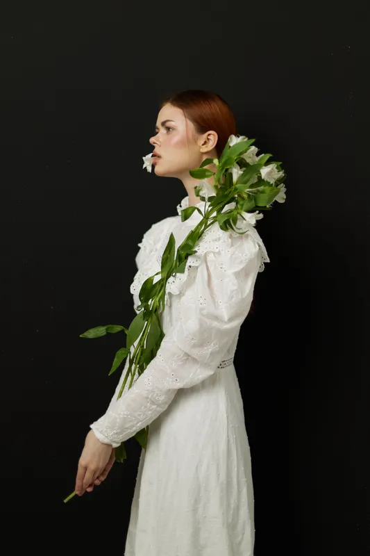 Beautiful woman in a white dress holding flowers against a dark background, embodying elegance and serenity with a touch of spring freshness